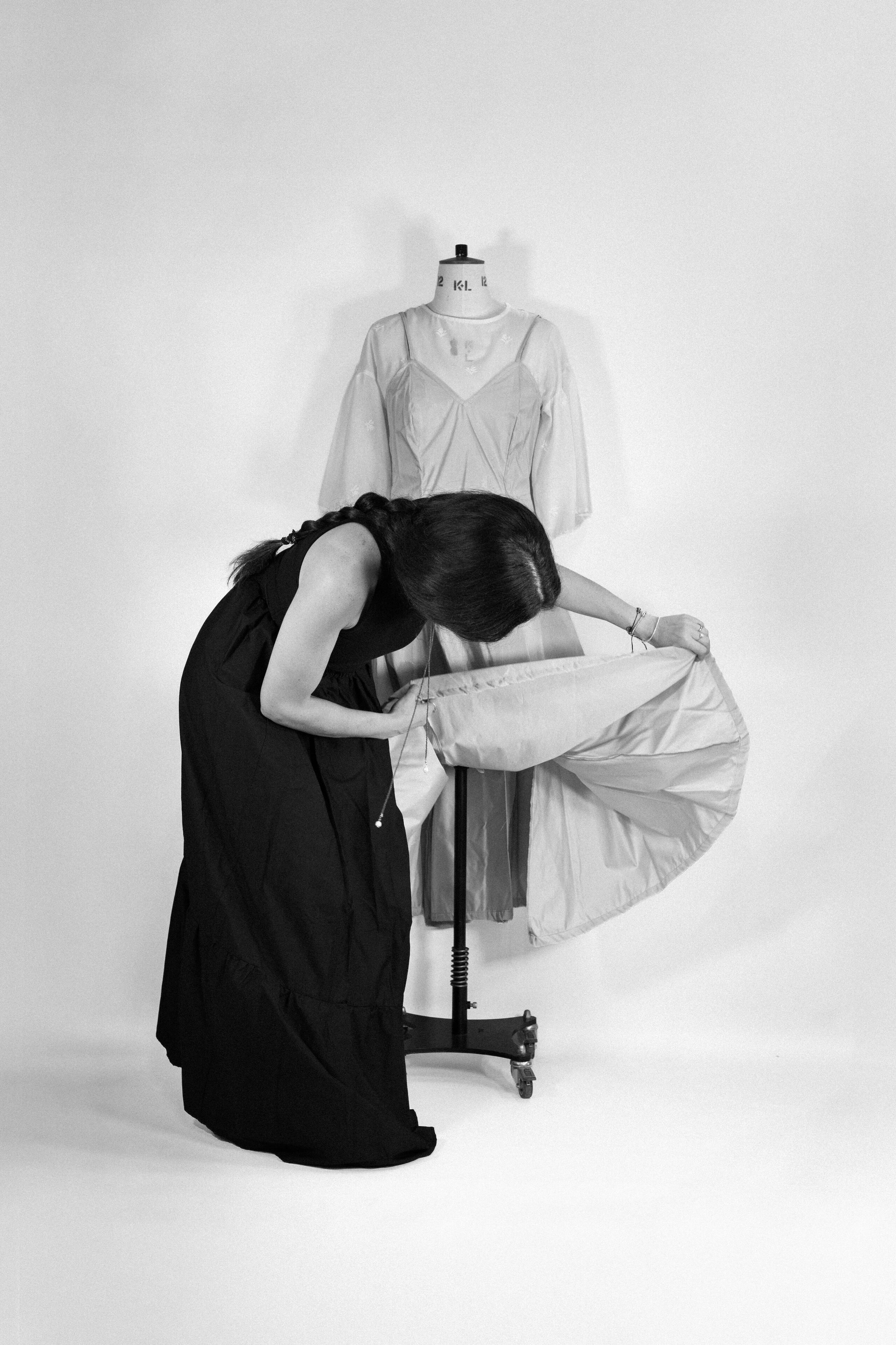 Alina Stanila | Fashion Designer at Work British fashion designer Alina Stanila examining the construction of a white garment on a dress form in her studio.